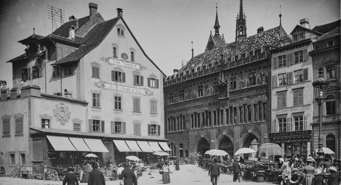 Schwarz-Weiss-Foto des Rathauses um 1880, noch ohne Turm und halb verdeckt durch das Haus zum Pfaueneck auf dem Marktplatz. 